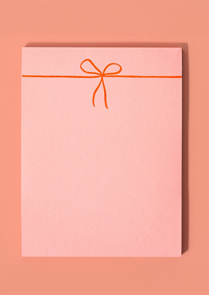A pink notepad with neon orange printed bow.