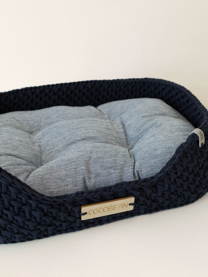 Navy woven pet bed with a gray cushion and personalized name tag