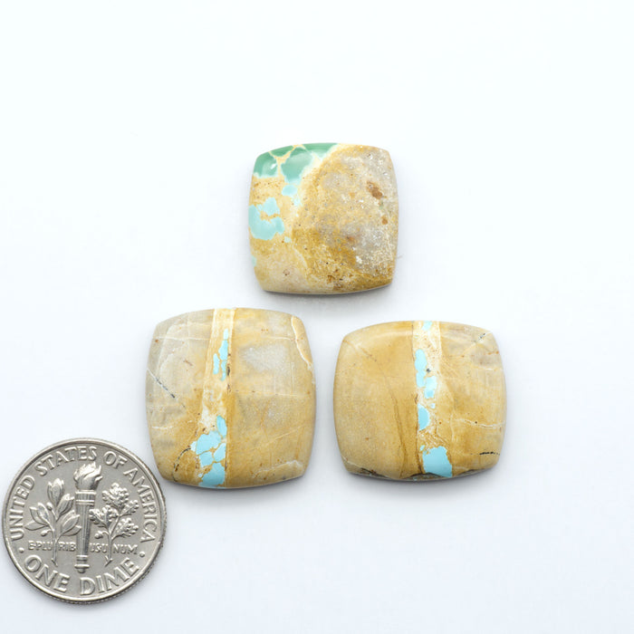 Three square royston stones with turquoise inclusions next to a U.S. dime dollar coin on a white background