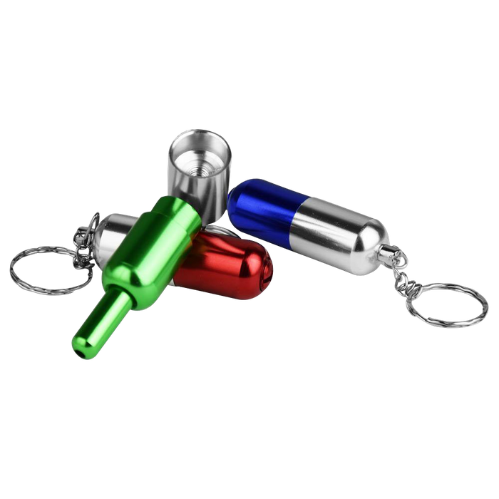 Angled close-up of three brightly anodized Pill Transformer Metal Hand Pipe keychain capsules in green, red and blue on a white background