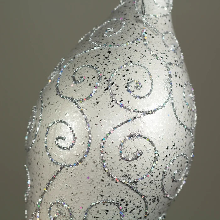 A close-up of a silver sprinkle finial ornament or vase-like object with an iridescent glitter swirl pattern on a soft beige background.