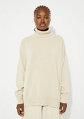 A woman wearing an oversized turtleneck sweater in beige.