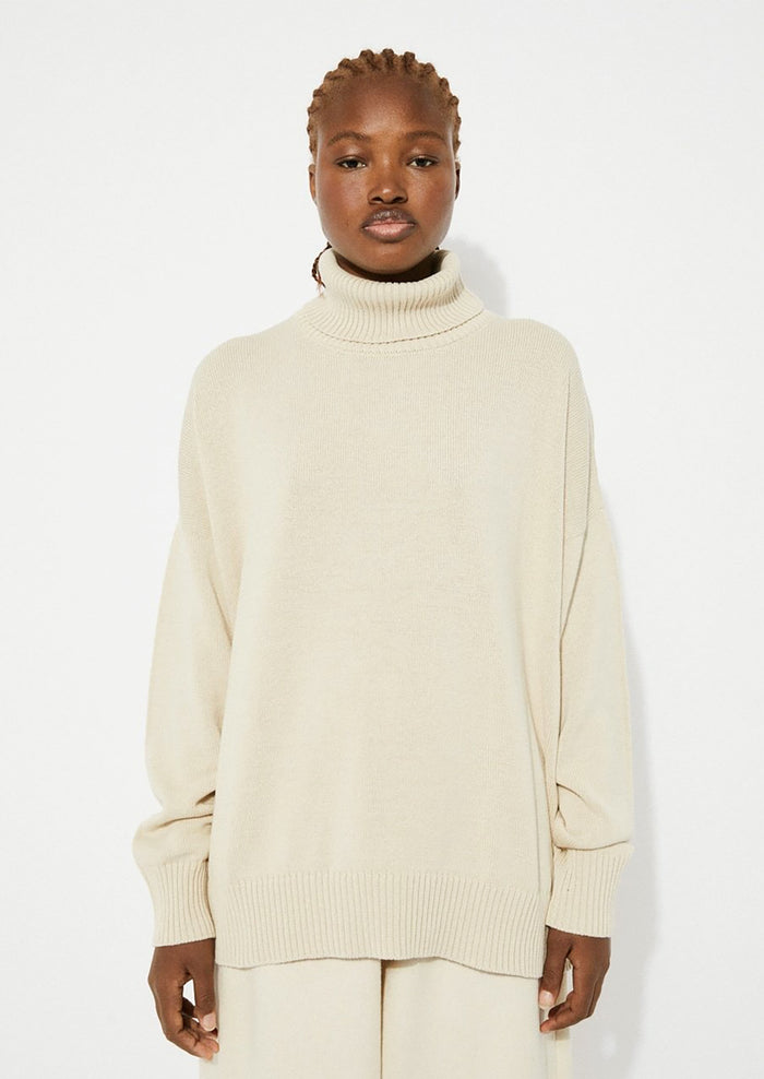 A woman wearing an oversized turtleneck sweater in beige.