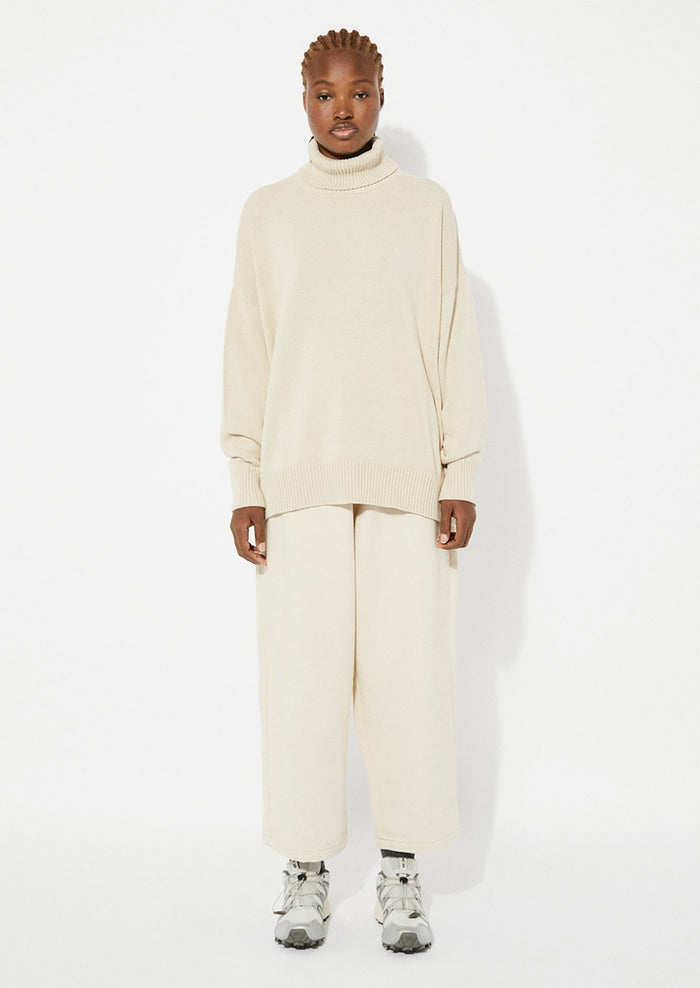 A woman wearing an oversized turtleneck sweater in beige.